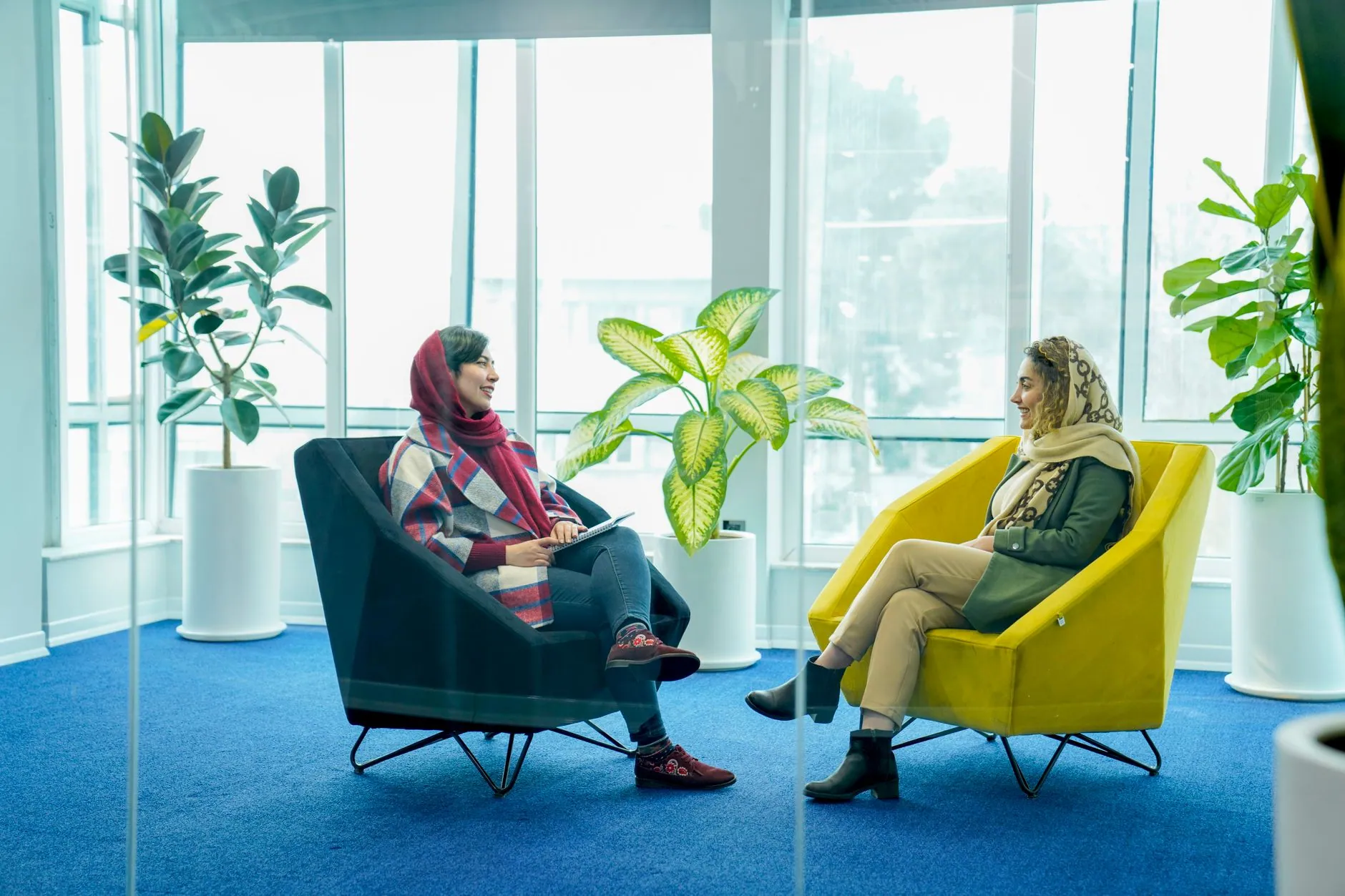 Two women talking in a bright room full of plants