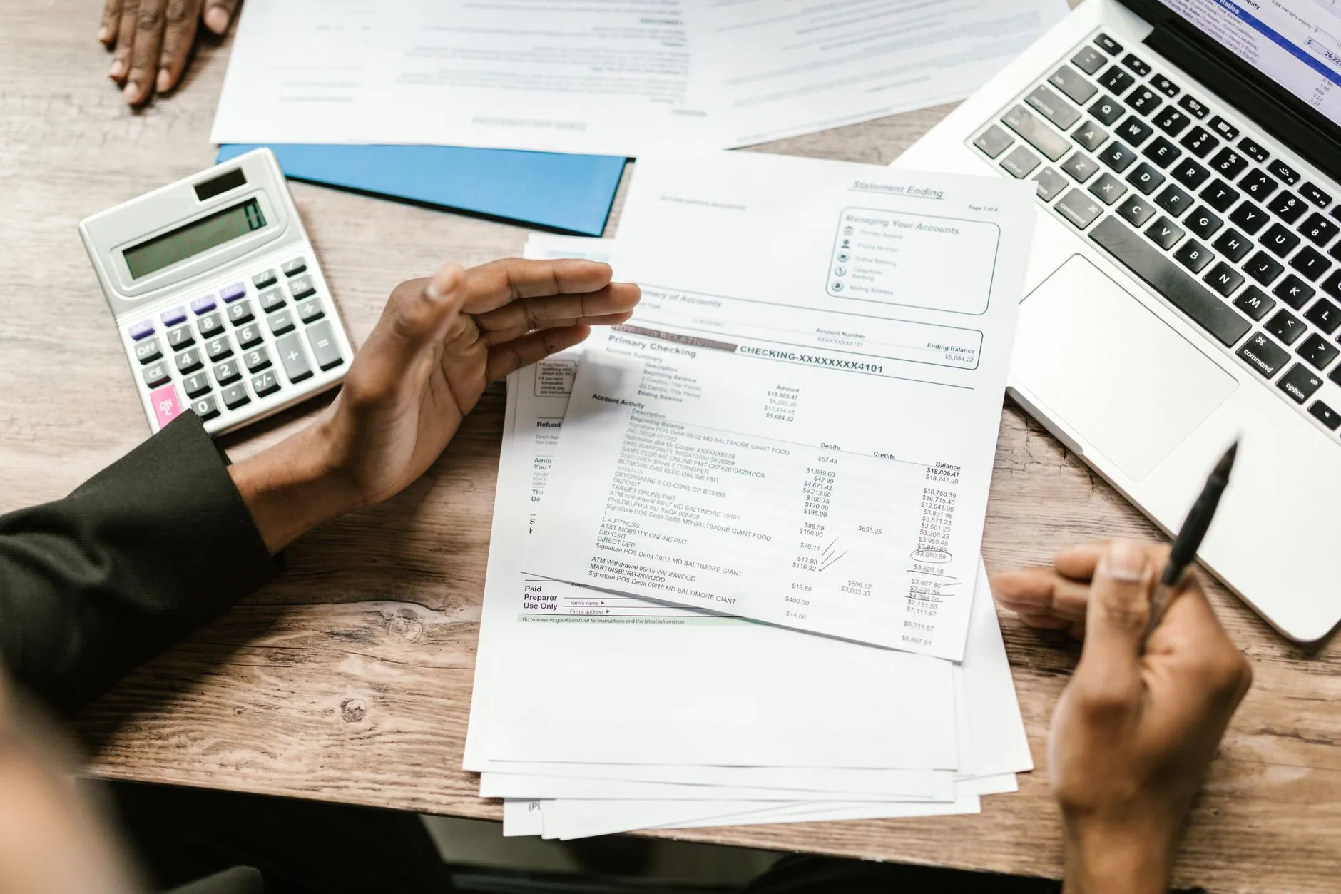 Hands reviewing invoices beside a calculator and a laptop